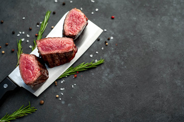 Three slices of grilled steak over meat knife with spices on a stone background with copy space for your text