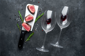 Three slices of grilled steak over a meat knife with spices and a bottle of red wine and glasses on a stone background. dinner for two