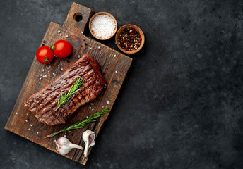 grilled beef steak on a wooden board with spices on a stone background with copy space for your text