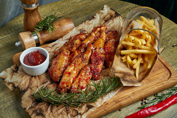 Great beer snack - spicy baked buffalo wings. BBQ wings with garnish of french fries on a wooden tray. Top view, food flat lay. Pub food