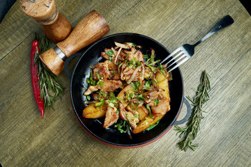 Fried potatoes with bacon, onions and herbs in a decorative pan on a wooden background. Top view on tasty food.