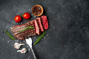 grilled beef steak on a meat fork with spices on a stone background with copy space for your text