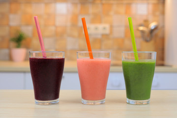 Glass with three smoothie and straw, on the kitchen, close-up