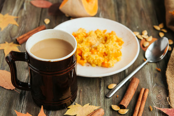  Vintage brown mug of tea or coffee on a background of pumpkins and plate with pumpkin porridge on an old wooden table. Cinnamon sticks.