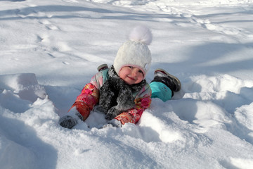 Fototapeta na wymiar Little girl posing lying on the snow and smiling