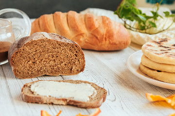  Loaf of rye bread and a sandwich with butter on a white wooden table.