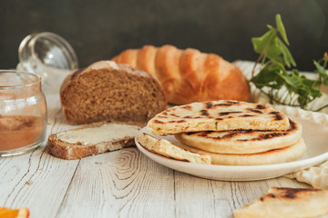  Potato cakes on a white plate against the background of loaves of bread on a white wooden table.