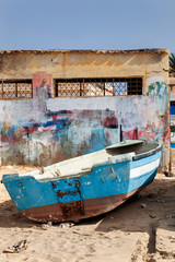 Fototapeta na wymiar Old weathered boat parked on the beach sand of Sal Rei with colorful building in the background on Boa Vista in Cape Verde