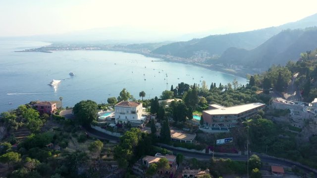 Cinematic landscape view of the blue sea bay with ships and shining water. A coast surrounded by the mass mountains fading in the fog. As drone descends, the panorama hides behind the hill