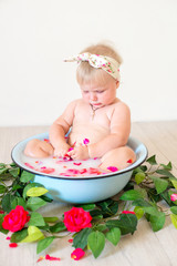 Little cute baby girl is sitting in a basin with pink petals and strawberries.