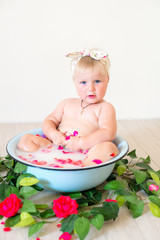 Little cute baby girl is sitting in a basin with pink petals and strawberries.