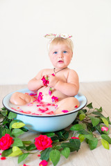 Little cute baby girl is sitting in a basin with pink petals and strawberries.