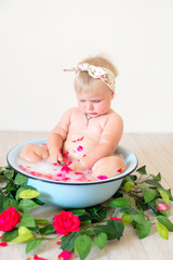 Little cute baby girl is sitting in a basin with pink petals and strawberries.