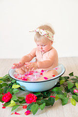 Little cute baby girl is sitting in a basin with pink petals and strawberries.