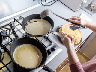 Batter pouring out of a metal bucket onto a red-hot greased frying pan. The process of baking pancakes.