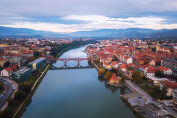 Aerial view of Maribor city in Slovenia on the banks of Drava river. Scenic landscape with buildings, embankment, historical bridge, mountains and blue cloudy sky, travel background, Lower Styria