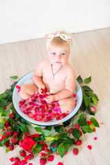 Little cute baby girl is sitting in a basin with pink petals and strawberries.