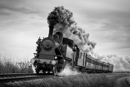 Steam train runs on the tracks on a cloudy day. Black and white photography. - Powered by Adobe