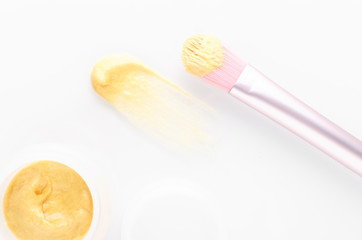 golden facial cream mask with a brush on white background