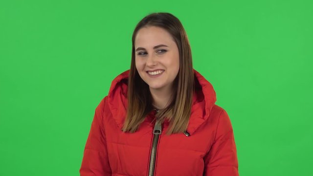 Portrait of lovely girl in a red down jacket is frightened then sighs with relief and smiling. Green screen