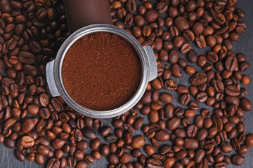 Coffee filter holder with and roasted beans scattered around on black background,