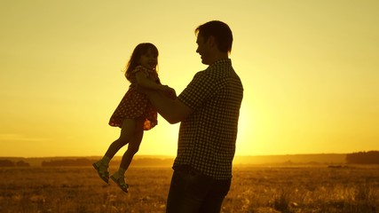 Dad beloved child in her arms dances in flight and laughs. Happy baby plays with his father at sunset. Silhouette of a man and a child. Family concept.