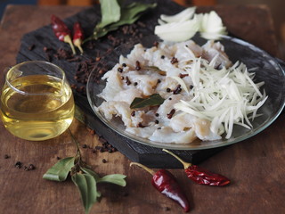 XE salad of freshly salted river pike fish on a cutting kitchen board with ingredients for cooking. Pike fillet pieces. Wooden brown background.