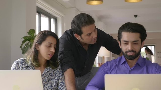 close up shot of a senior male executive and a young female and a young male junior executive colleagues engaged in a close discussion about work over a laptop in office