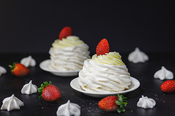  Pavlovа cake with strawberries on a white saucer, around meringues and strawberries,dark background