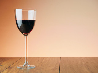 One glass of red wine on a wooden table, warm background color. Horizontal image.