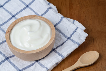 Natural homemade plain organic yogurt in wooden bowl and wood spoon on wood texture background