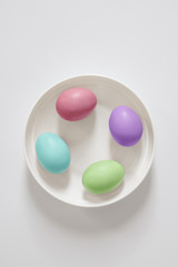 Four multicolored easter eggs lie on a white plate on a light white background.  Copy space for your text