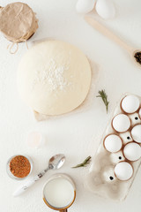 Ingredients for cooking on a white background, including milk, eggs, spices and dough with a rolling pin and black pepper with polka dots. The concept of cooking and recipes.