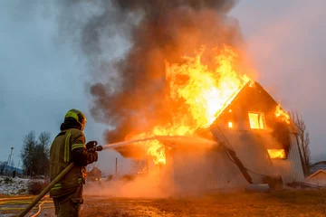 Tuinposter Norwegian firefighter trying to put out flames house on fire © STUEDAL