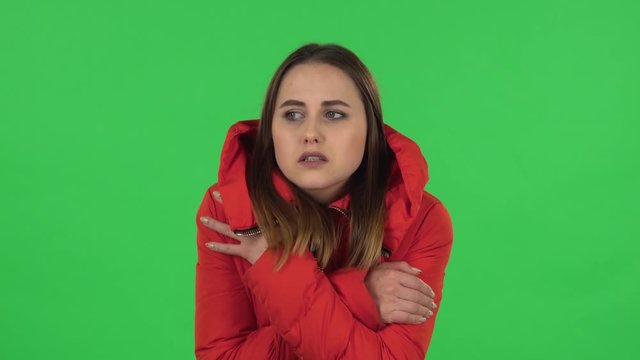 Portrait of lovely girl in a red down jacket froze and trying to keep warm. Green screen