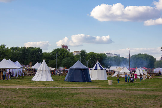 people at the festival of medieval culture with tents and bonfires in the green forest on the background of the modern city