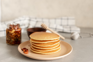 Stack of delicious pancakes with chocolate, honey, nuts and slices of banana on plate and napkin on wooden background