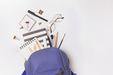 Backpack with different stationery and study supplies on the white background