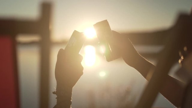 Close up shot of two people toasting with cans during sunset while sitting in their deck chairs