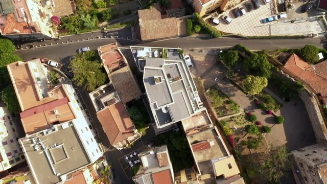 Flying across a small Italian resort town with tiny orange old buildings, churches, fountains, tennis courts, swimming pools, and other attractions. Top down view. Taormina, southern Italy