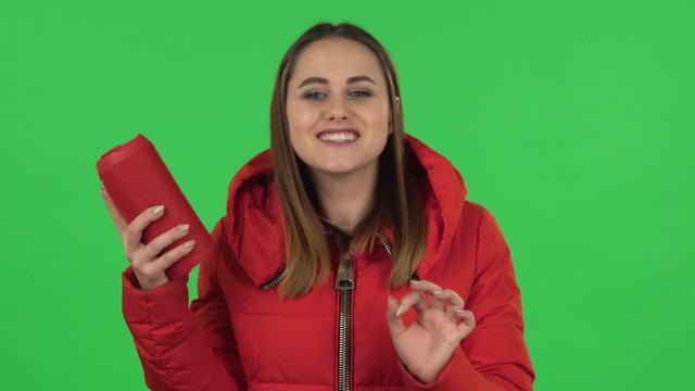 Portrait of lovely girl in down jacket is listening to music with bluetooth portable speaker and dancing. Green screen