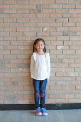 Portrait of happy asian little girl with pigtail hair in jeans and a white shirt standing at brick wall background