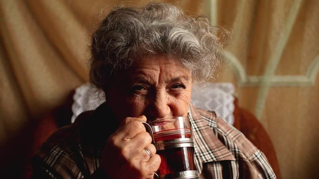 Elderly happy woman smile and drink tea from glass and old cup