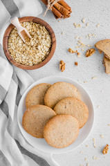 Freshly baked oatmeal cookies with raisins and nuts on a white plate on a light stone background. Rustic style Vertical orientation. Top view.