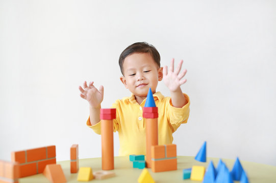 Cheerful asian little baby boy playing a colorful wood block toy on table over white background.