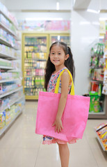 Attractive little asian girl carrying a pink recycle bag (spun ball bag) while go to retail stores. Eco friendly bag for reduce or zero waste concept.