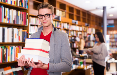 student standing in library with pile of books