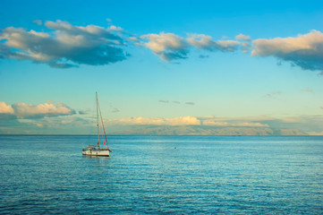 Fototapeta premium A small boat bobs on the surface of a calm sea. Dawn over the ocean. Colorful sky and calm ocean. An island is visible in the distance.