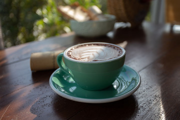 Fototapeta na wymiar A green cup of coffee placed on a wooden table by the window in a coffee shop, Concept: Delicious breakfast drinks fragrant suitable for lifestyle, closeup cup of coffee over the top with space