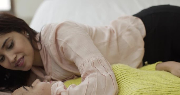 Handheld shot from face to the feet of two best female friends forever lying down on bed and sharing gossip and other secret information with each other as they chat and also touch each other intimate